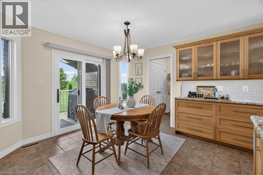Light-toned cabinetry with glass-front uppers, a subway tile backsplash, and a sliding glass door to the exterior - 515 Woodward Drive, Mount Brydges, ON