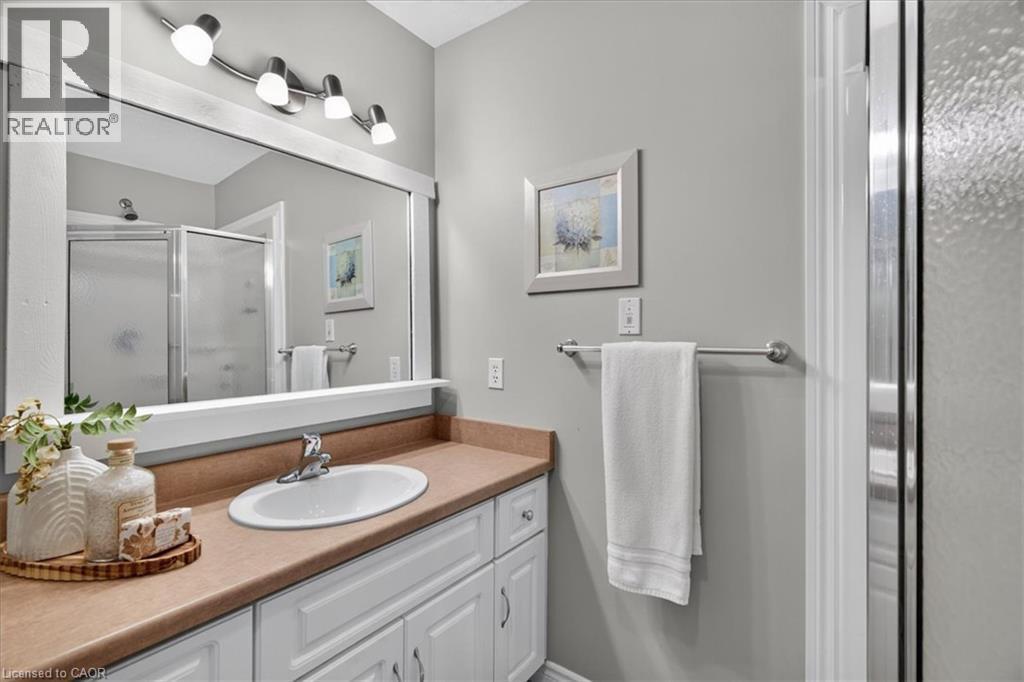 White vanity with integrated sink, brushed nickel faucet, large framed mirror, track lighting, and a glass-enclosed shower - 515 Woodward Drive, Mount Brydges, ON
