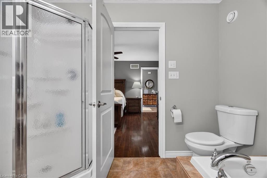 Enclosed shower with textured glass, white toilet, and brown tile flooring - 515 Woodward Drive, Mount Brydges, ON
