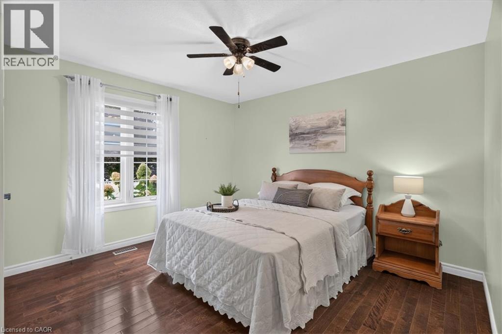 Rich wood-finish flooring, a ceiling fan with integrated lighting, and a window with blinds and sheer drapes - 515 Woodward Drive, Mount Brydges, ON