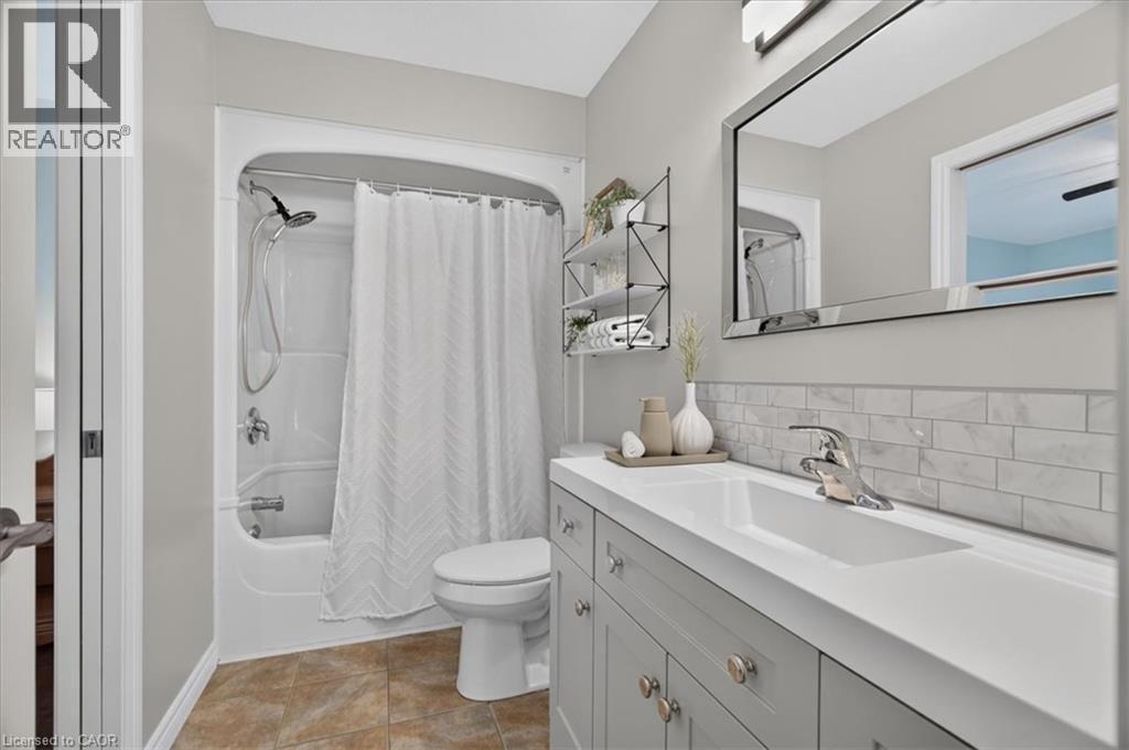 White subway tile backsplash, integrated rectangular sink, chrome faucet, mirrored vanity, and light gray vanity cabinetry - 515 Woodward Drive, Mount Brydges, ON