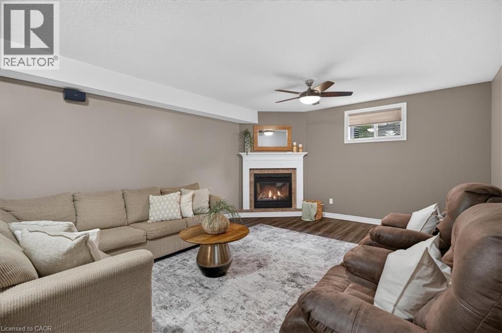 Corner fireplace with a white mantel, wood-finish flooring, and a ceiling fan - 515 Woodward Drive, Mount Brydges, ON