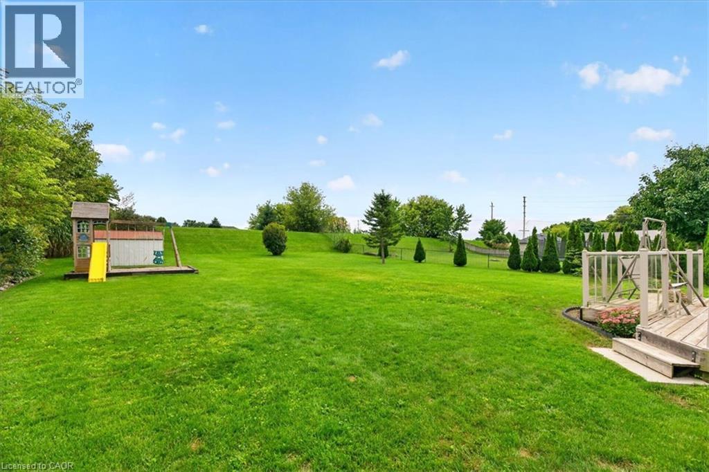 Expansive green lawn with mature trees, established landscaping, and a multi-level wooden deck - 515 Woodward Drive, Mount Brydges, ON