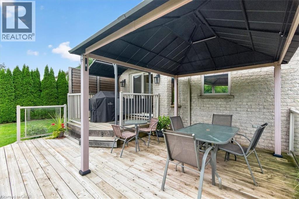 Expansive wood-finish deck with a built-in privacy wall, glass panel railings, and a two-tier design - 515 Woodward Drive, Mount Brydges, ON