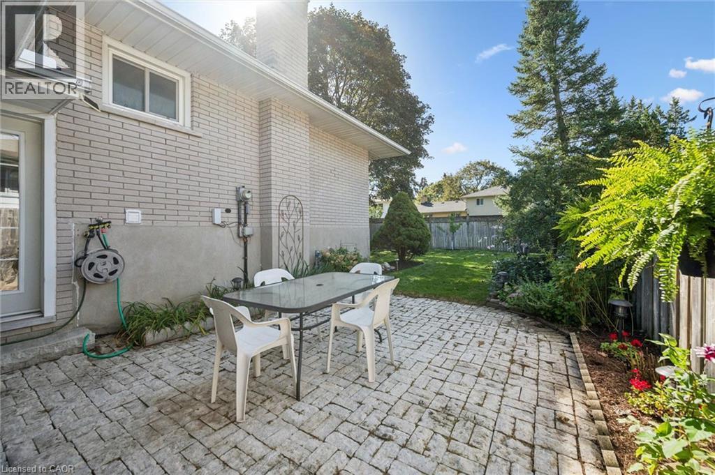 Expansive brick paver patio with a manicured lawn area, bordered by mature trees and established garden beds - 35 Crosby Drive, Kitchener, ON