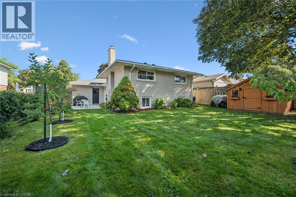Expansive rear yard featuring green lawn, a light brick exterior, a patio with direct access, a detached wooden shed, and a privacy fence - 35 Crosby Drive, Kitchener, ON