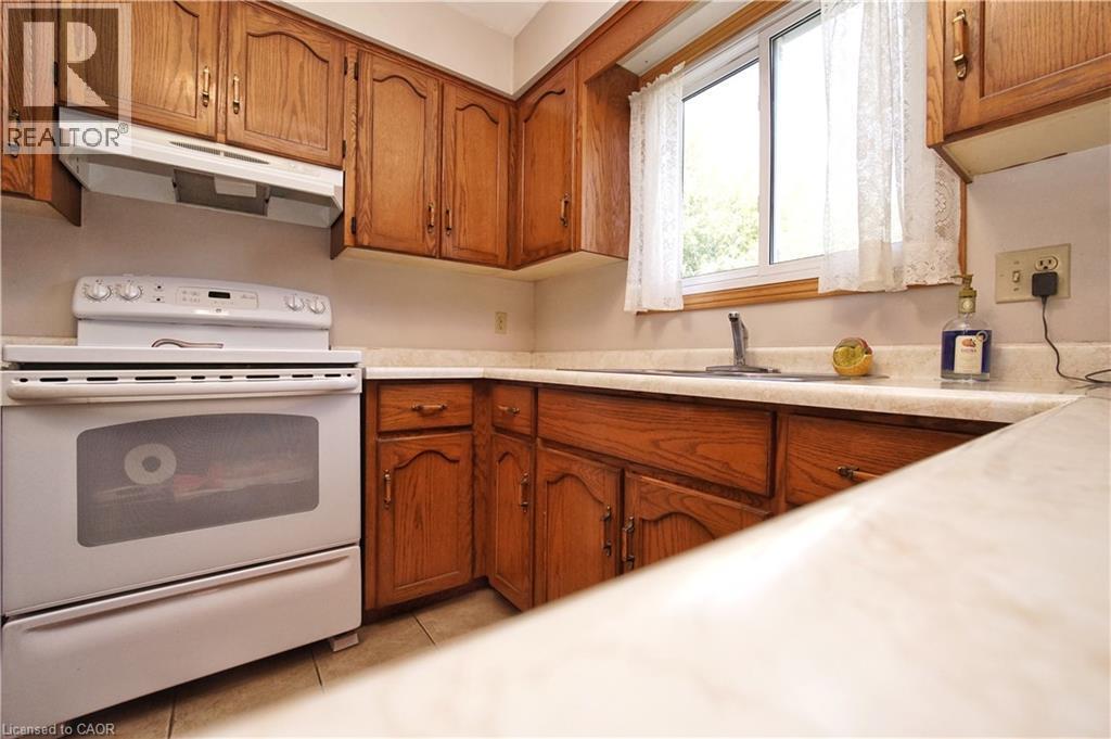 Wood-finish cabinetry, white range, built-in range hood, light-colored countertops, and window over sink - 56 Scenic Wood Crescent, Kitchener, ON