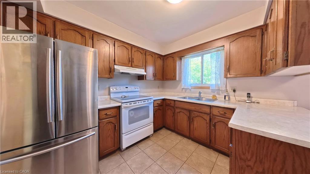 Kitchen featuring wood cabinetry, white countertops, a stainless steel refrigerator, and tiled flooring - 56 Scenic Wood Crescent, Kitchener, ON
