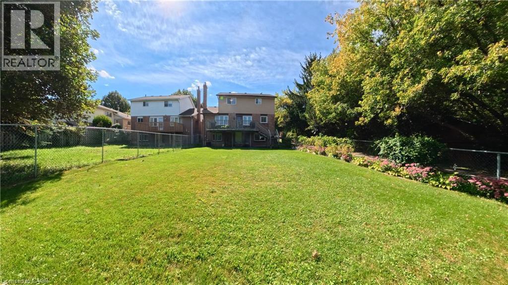 Expansive backyard with a green lawn, mature trees, and a garden bed - 56 Scenic Wood Crescent, Kitchener, ON