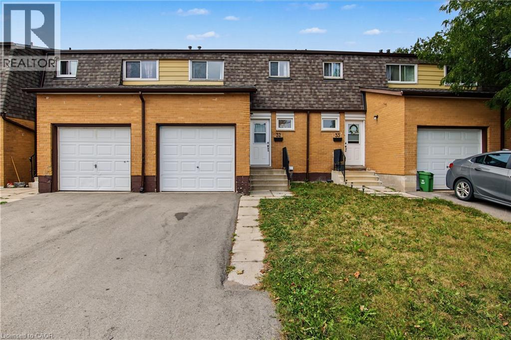 Brick exterior with a mansard roof, multiple windows, and individual garage doors - 1444 Upper Ottawa Street Unit# 32, Hamilton, ON