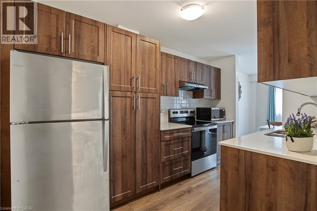 Contemporary kitchen featuring wood-finish cabinetry, stainless steel appliances, white subway tile backsplash, and light-toned countertops - 1444 Upper Ottawa Street Unit# 32, Hamilton, ON