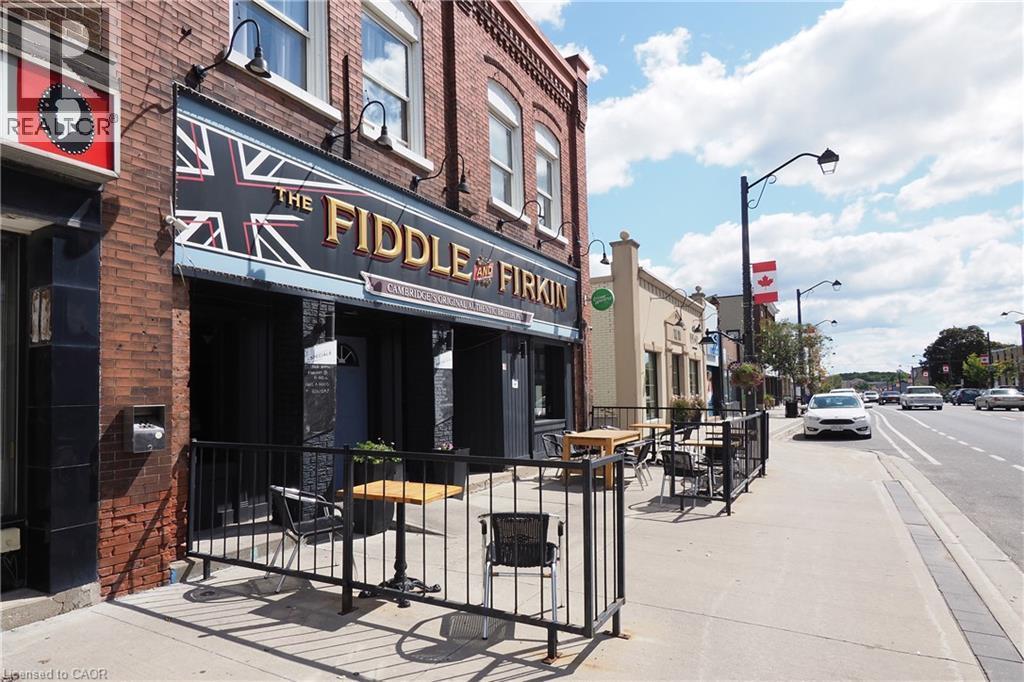 Brick facade commercial building with a prominent storefront, exterior lighting fixtures, and an outdoor patio area enclosed by black railings - 707 E King Street E, Cambridge, ON