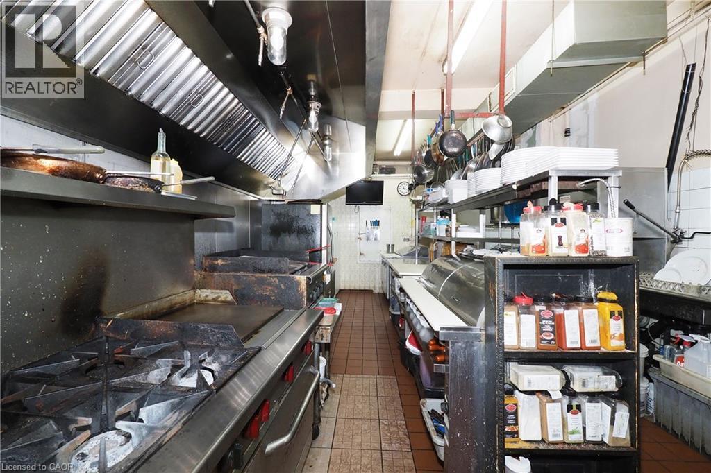 Commercial kitchen featuring stainless steel range hood, multiple cooking surfaces, and built-in shelving - 707 E King Street E, Cambridge, ON