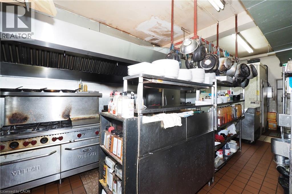 Commercial kitchen featuring a stainless steel range with a ventilation hood, tiled flooring, and extensive metal shelving - 707 E King Street E, Cambridge, ON