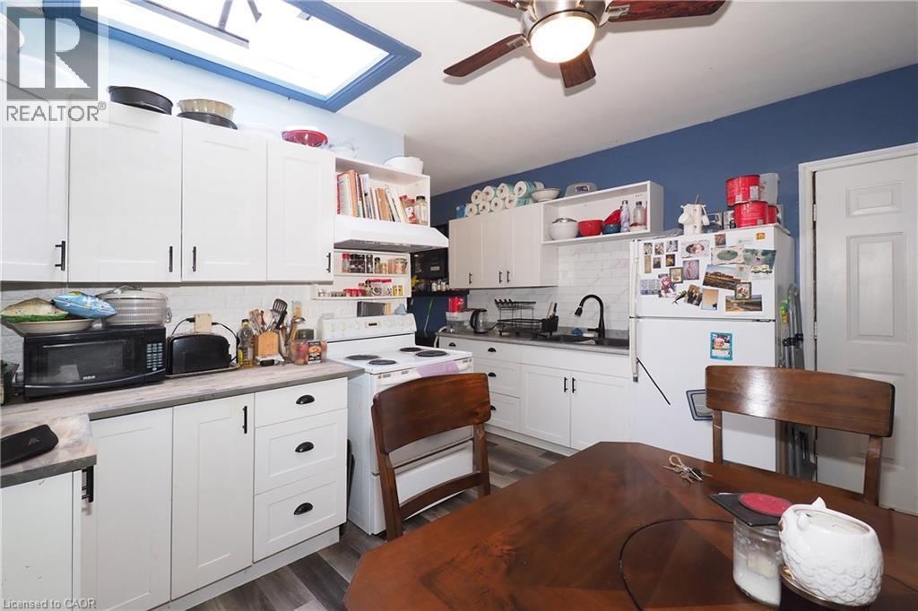 Kitchen featuring white cabinetry, a skylight, wood-finish flooring, a ceiling fan, and solid surface countertops - 707 E King Street E, Cambridge, ON