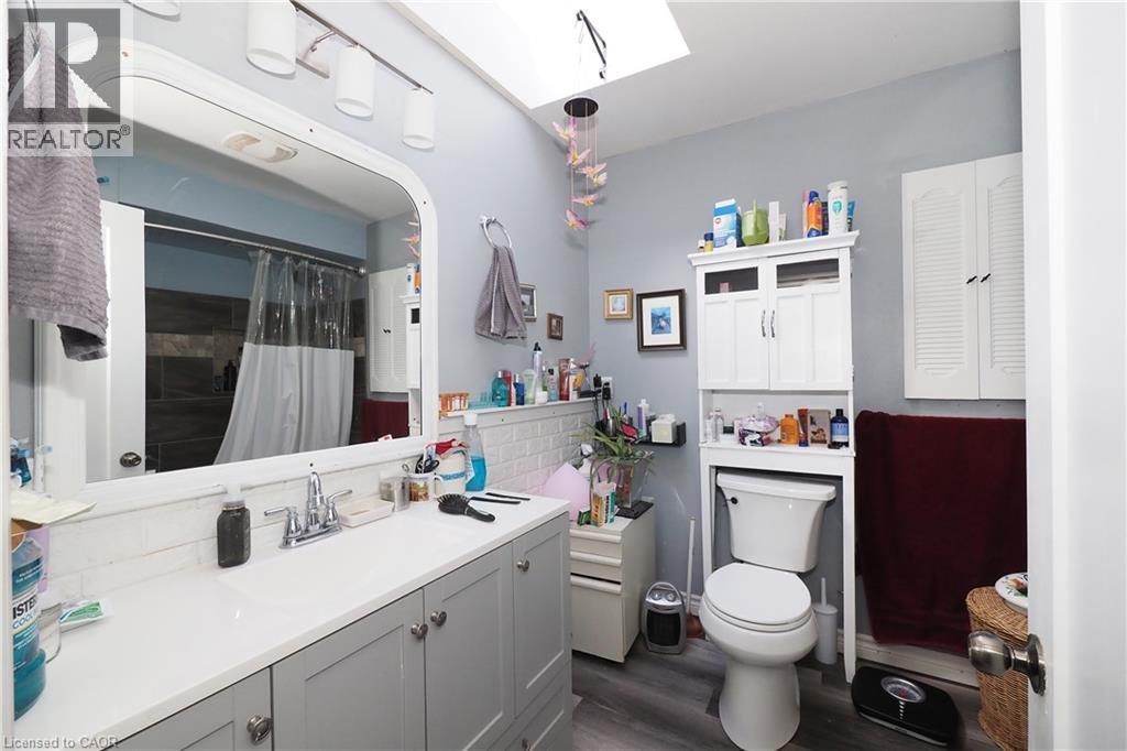 Vanity with an integrated sink, track lighting, wood-finish flooring, white wall cabinetry, and a skylight - 707 E King Street E, Cambridge, ON