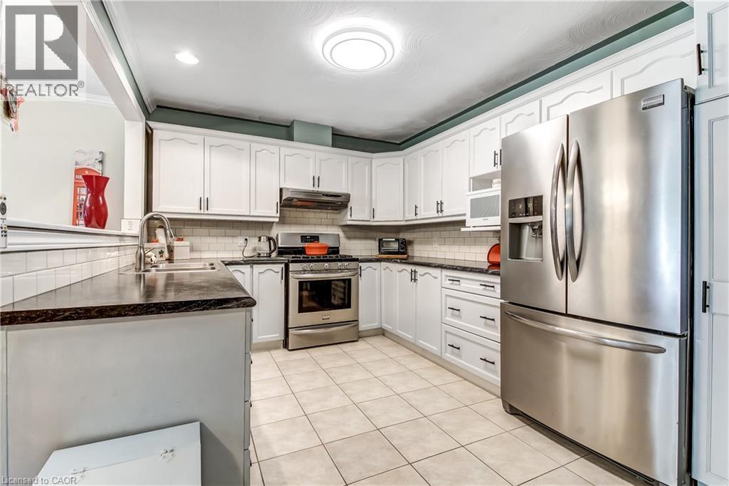 White cabinetry, stainless steel appliances, dark countertops, tile backsplash, and tile flooring - 150 Oak Street Unit# 27, Simcoe, ON