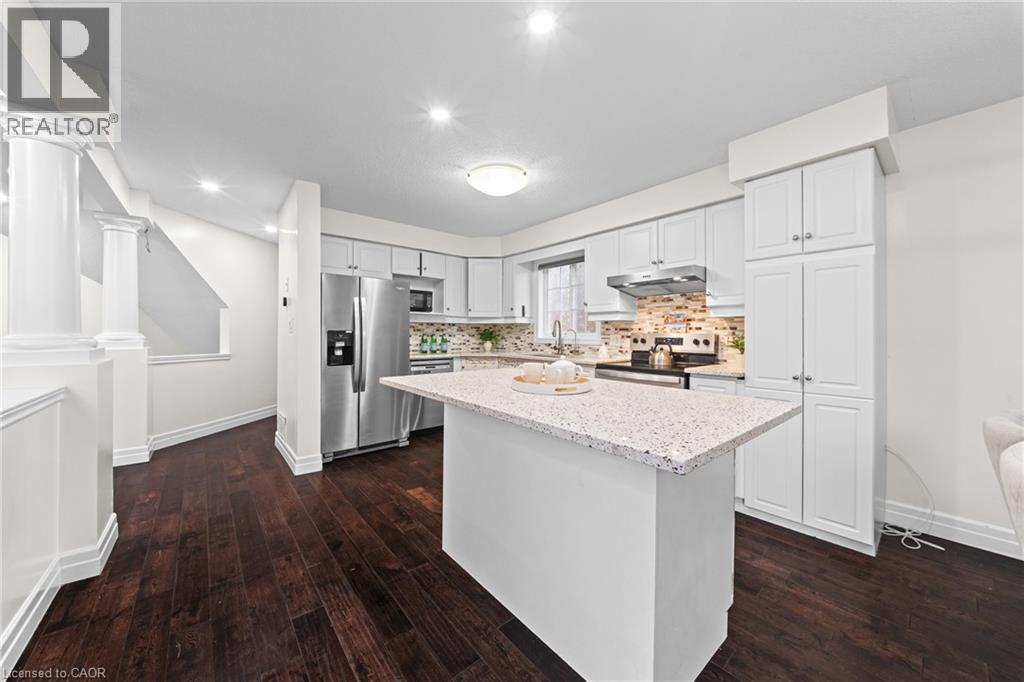 Kitchen featuring a center island with a light-toned countertop, white cabinetry, stainless steel appliances, and a tiled backsplash - 495 Brigantine Drive, Waterloo, ON