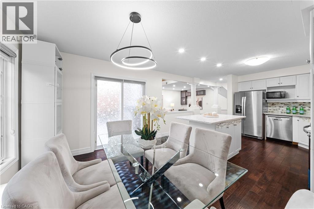 Open-concept dining area featuring a contemporary lighting fixture, wood-finish flooring, and white built-in cabinetry - 495 Brigantine Drive, Waterloo, ON