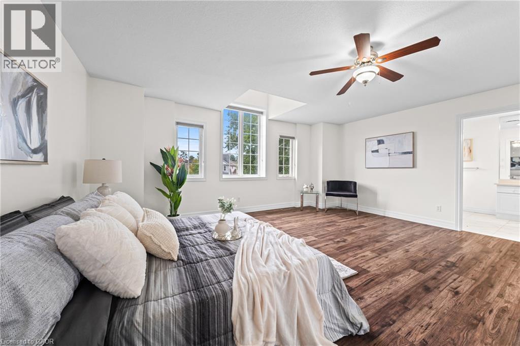 Spacious room featuring wood-finish flooring, multiple windows, a ceiling fan with integrated lighting, and an open doorway to a bathroom with tile flooring - 495 Brigantine Drive, Waterloo, ON