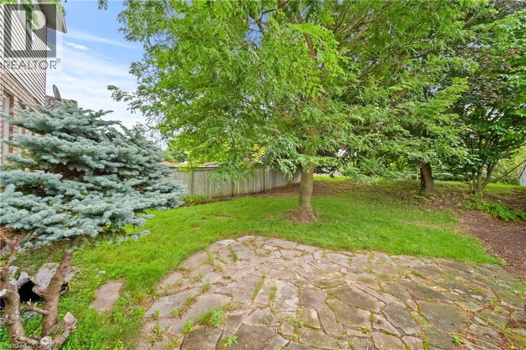 Expansive outdoor space featuring a flagstone patio, mature trees, and a privacy fence - 495 Brigantine Drive, Waterloo, ON