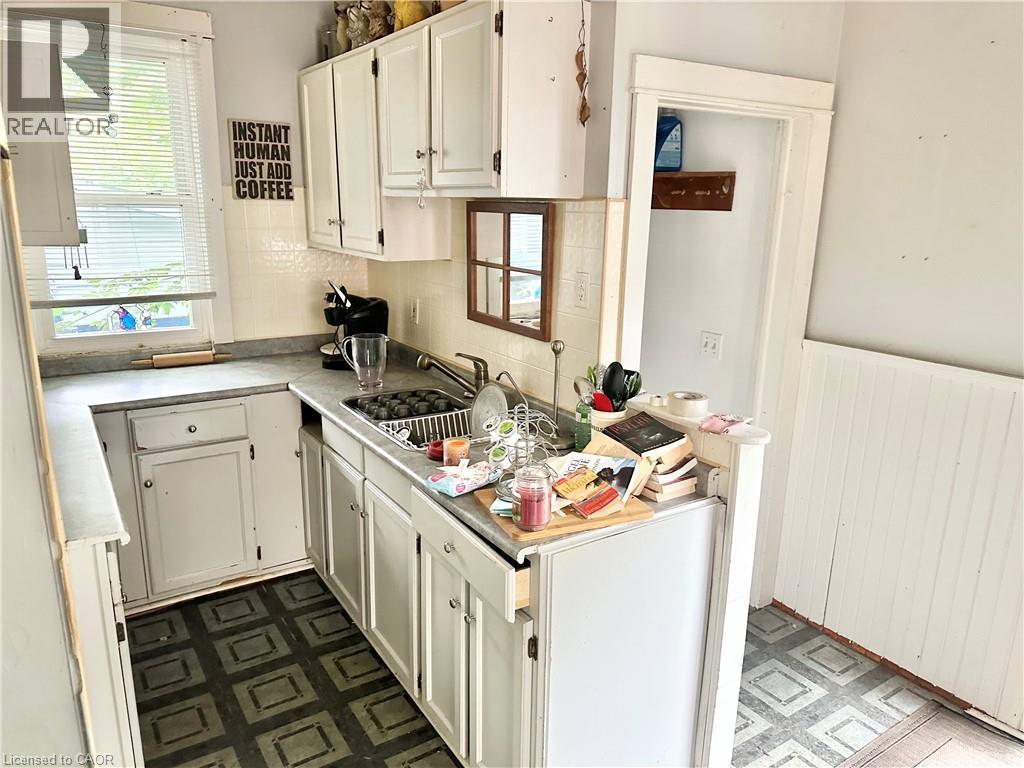 Kitchen featuring white cabinetry, a stainless steel sink, tiled backsplash, and patterned floor - 128 Kent Street S, Simcoe, ON