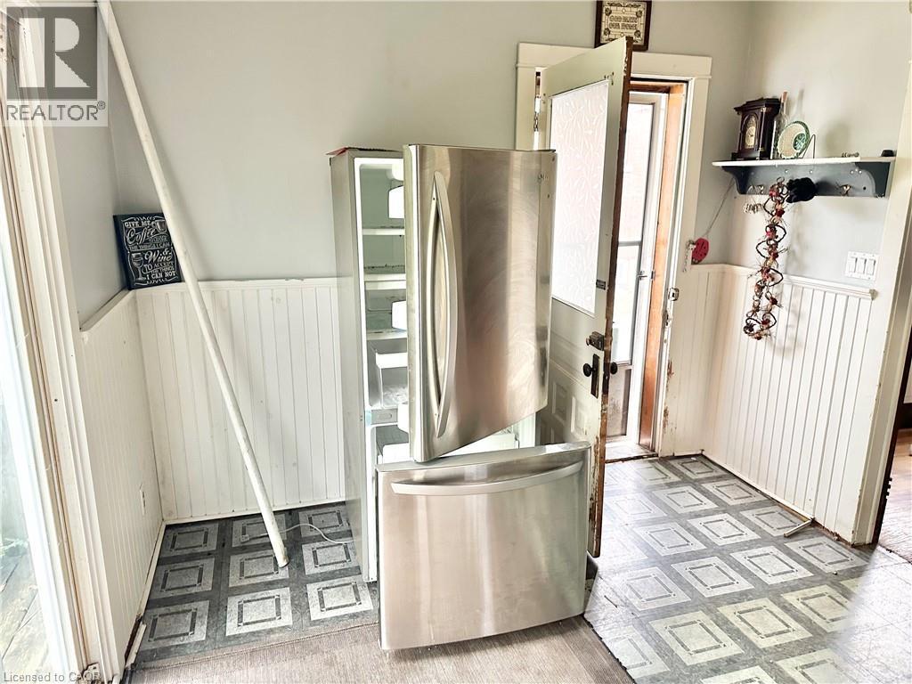 Another angle of the Kitchen -Stainless steel French door refrigerator, beadboard paneling, patterned flooring, and a white interior door - 128 Kent Street S, Simcoe, ON
