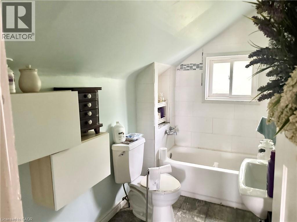 White bathtub with tile surround and built-in storage niche, single-pane window, and wall-mounted sink - 128 Kent Street S, Simcoe, ON