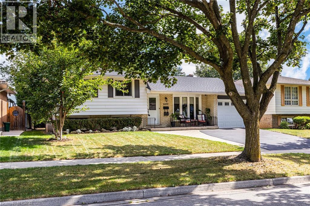 Exterior featuring light brick and white siding, an attached garage, a paved driveway, and a front porch with a white railing - 2037 Mountain Grove Avenue, Burlington, ON