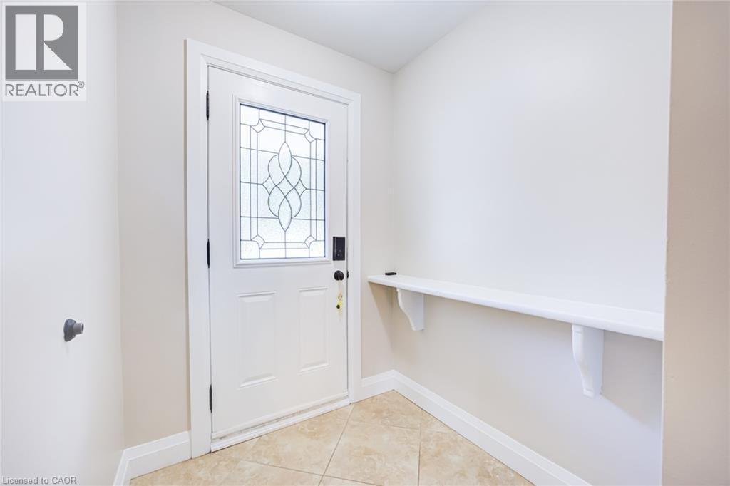 Entryway featuring a white door with decorative glass inserts, ceramic tile flooring, a built-in shelf, and neutral wall tones - 2037 Mountain Grove Avenue, Burlington, ON