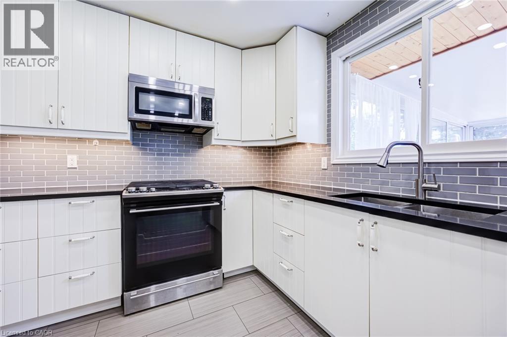 White upper and lower cabinetry, dark countertops, subway tile backsplash, stainless steel appliances, and a window with a sink and modern faucet - 2037 Mountain Grove Avenue, Burlington, ON