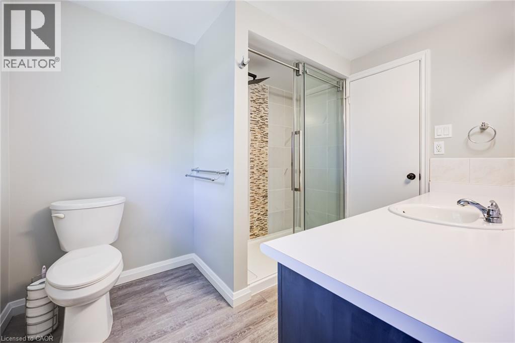 Wood-finish flooring, white vanity with integrated sink, glass-enclosed shower, shower with mosaic tile accent, and white toilet - 2037 Mountain Grove Avenue, Burlington, ON