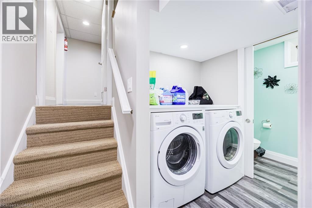 Carpeted staircase with white handrail, recessed lighting, and laundry area featuring front-loading washer and dryer - 2037 Mountain Grove Avenue, Burlington, ON
