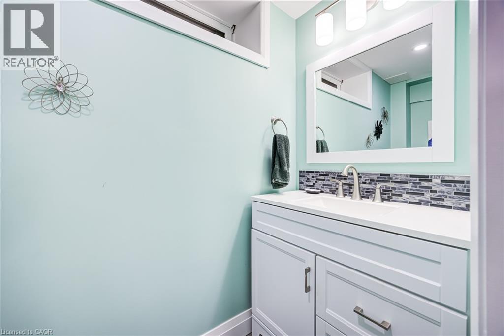 White vanity with integrated sink, mosaic tile backsplash, framed mirror, and wall-mounted light fixture - 2037 Mountain Grove Avenue, Burlington, ON