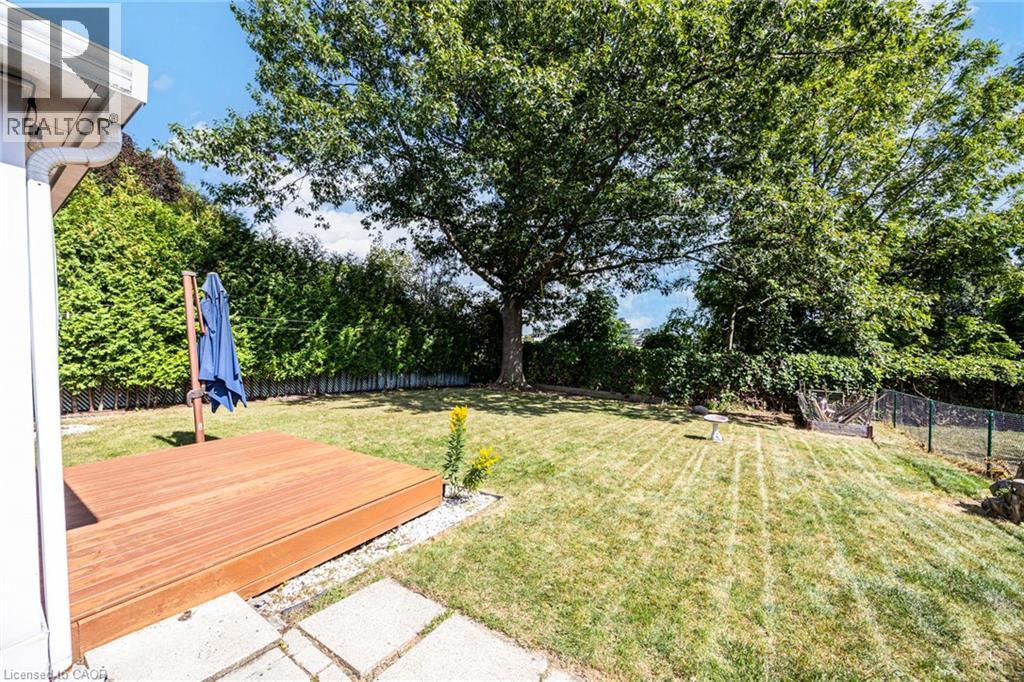 Expansive backyard featuring a grass lawn, mature trees, a wood-finish deck, and stone paver steps - 2037 Mountain Grove Avenue, Burlington, ON
