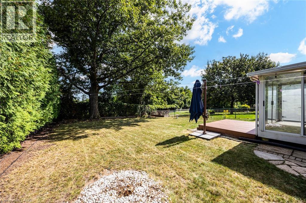 Expansive grassy yard with mature trees, a wooden deck, and a sunroom featuring large glass sliding doors - 2037 Mountain Grove Avenue, Burlington, ON