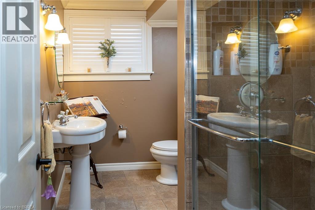 Pedestal sink with chrome fixtures, wall-mounted light fixtures, tile flooring, and a glass-enclosed shower - 78 Berkley Crescent, Simcoe, ON