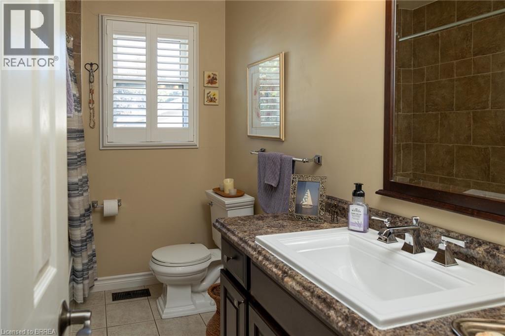 White plantation shutters, full vanity with integrated sink, chrome dual-handle faucet, dark wood-finish vanity cabinetry, and a walk-in shower with brown tile surround - 78 Berkley Crescent, Simcoe, ON