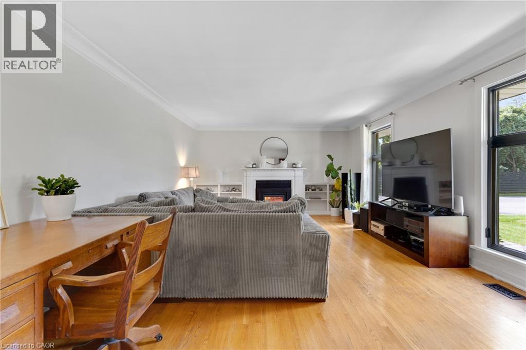 Hardwood flooring, crown molding, built-in fireplace with white mantel, white built-in shelving, and large windows - 7 Shadywood Lane, Cambridge, ON