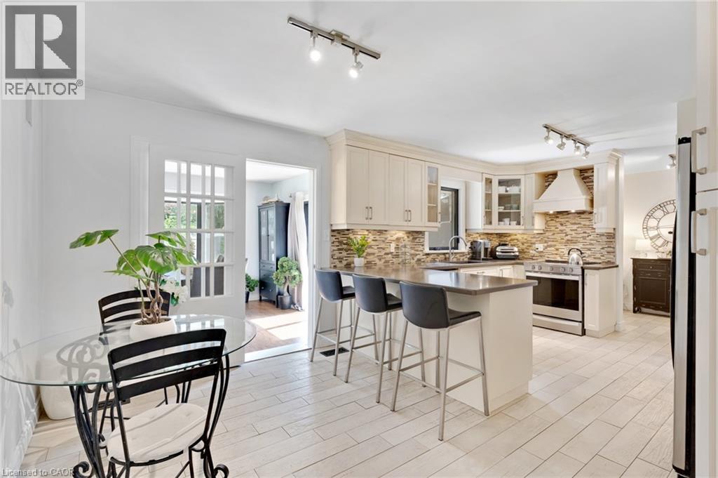Kitchen featuring light cabinetry, stainless steel appliances, stacked stone backsplash, and an island with countertop seating - 7 Shadywood Lane, Cambridge, ON