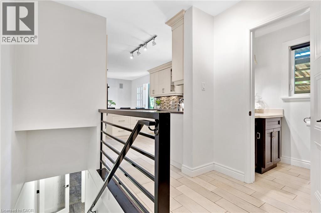 Modern black metal railing, light wood-finish flooring, white walls, and a powder room with a dark wood vanity and light countertop - 7 Shadywood Lane, Cambridge, ON