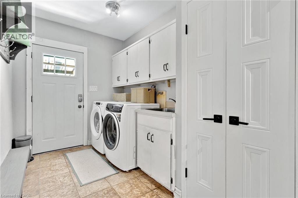Utility area featuring white paneled cabinetry, front-load washer and dryer, and a built-in sink with a countertop - 7 Shadywood Lane, Cambridge, ON