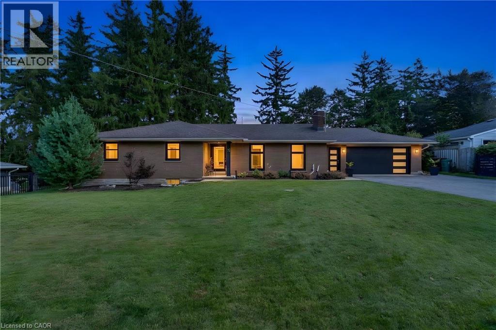 Brick exterior with a dark-pitched roof, modern garage door featuring horizontal glass panels, and a front entry with a prominent porch light - 7 Shadywood Lane, Cambridge, ON