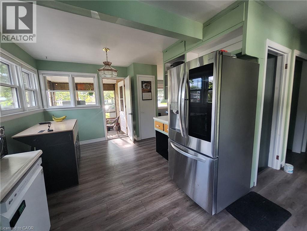 Spacious kitchen featuring stainless steel French-door refrigerator, wood-finish flooring throughout, soft-close cabinetry, and abundant natural light from multiple windows - 33 Lee Avenue, Simcoe, ON