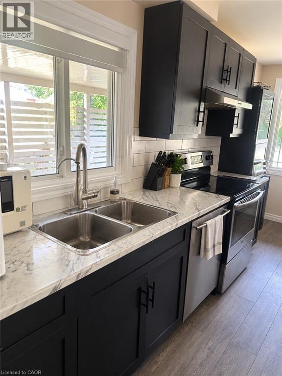 Black shaker-style cabinetry, white subway tile backsplash, stainless steel double basin sink, stainless steel appliances, and wood-finish flooring - 73 Larkspur Crescent, Kitchener, ON