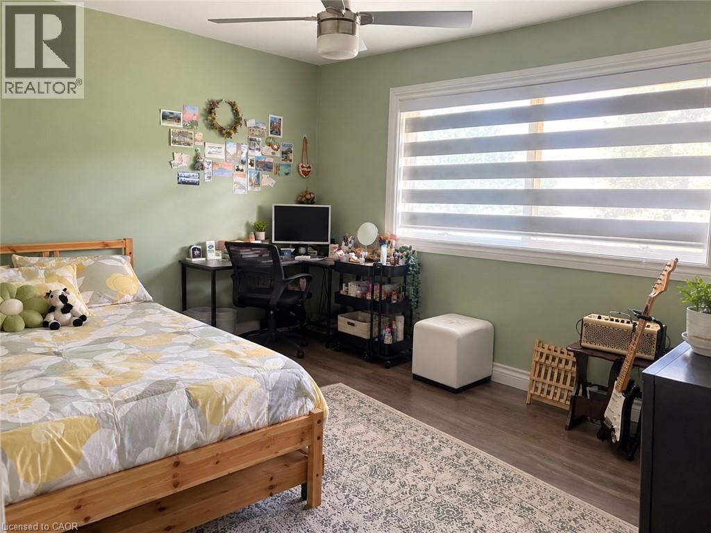 Wood-finish flooring, ceiling fan with integrated lighting, large window with layered blinds, light green wall finishes, and white trim - 73 Larkspur Crescent, Kitchener, ON