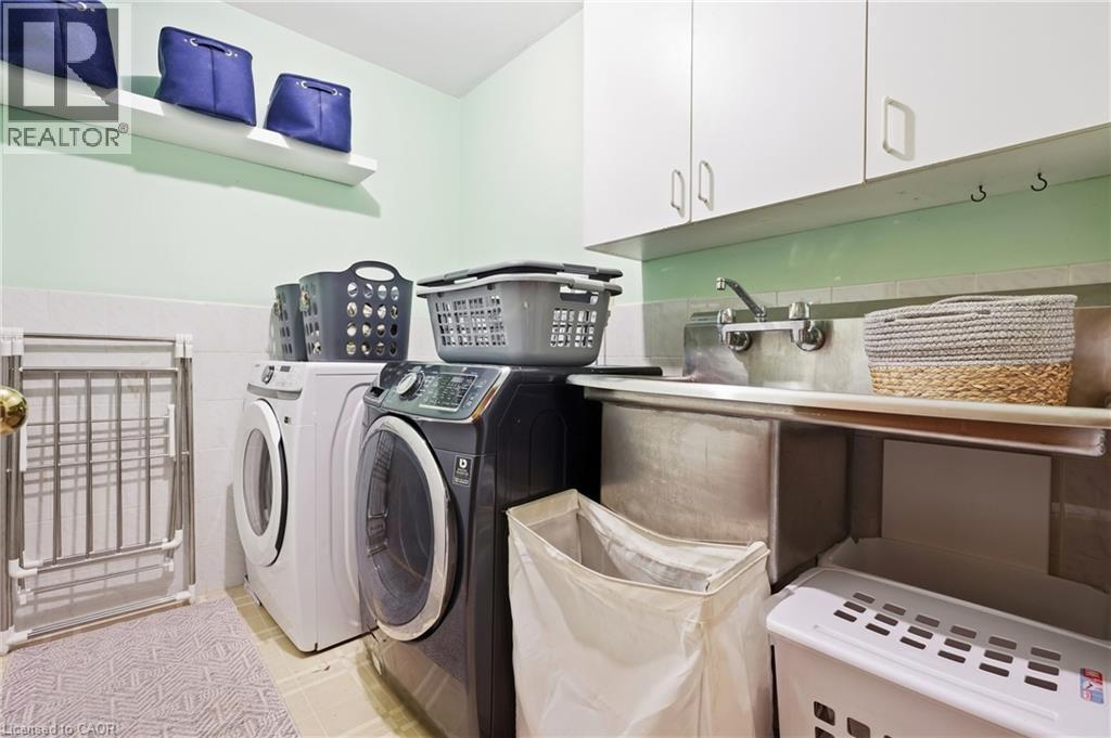Laundry area featuring white cabinetry, a stainless steel utility sink, wall-mounted faucet, and floating shelving - 76 Madeira Crescent, Cambridge, ON