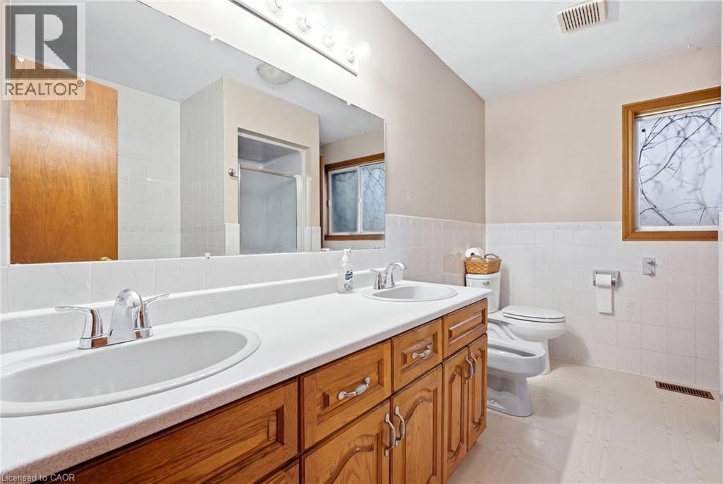 Dual vanity with chrome fixtures and integrated sinks, wood-finish cabinetry, full-width wall mirror, and white tiled wainscoting - 76 Madeira Crescent, Cambridge, ON
