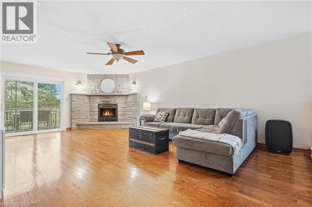 Corner stone fireplace, wood-finish flooring, ceiling fan, and sliding glass door with deck access - 76 Madeira Crescent, Cambridge, ON