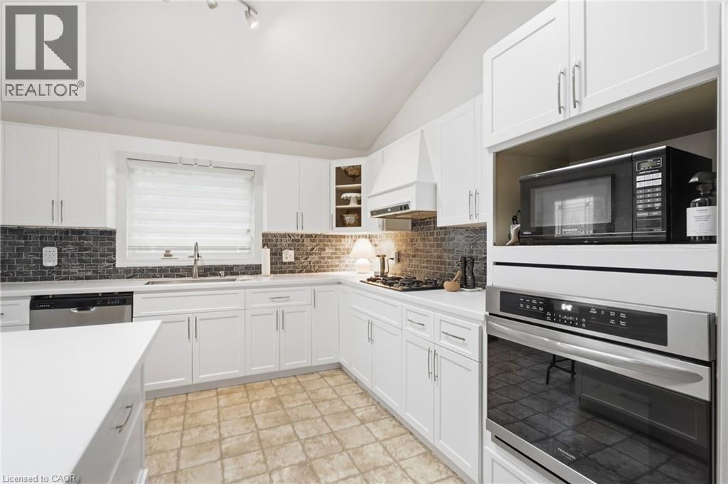 White cabinetry with stainless steel hardware, tile backsplash, built-in oven, and a vaulted ceiling - 76 Madeira Crescent, Cambridge, ON